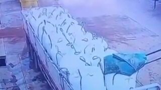 CCTV footage captures the moment a truck driver fell from the top of his vehicle while attempting to pull the truck cover over goods loaded by a forklift, slipping and injuring himself after losing his grip.