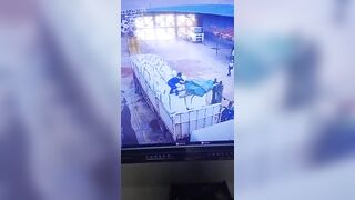 CCTV footage captures the moment a truck driver fell from the top of his vehicle while attempting to pull the truck cover over goods loaded by a forklift, slipping and injuring himself after losing his grip.