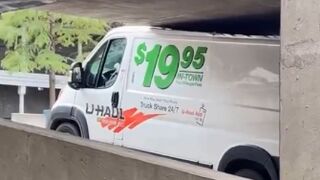 Man in a U-Haul van damaging the roof after driving into a parking garage